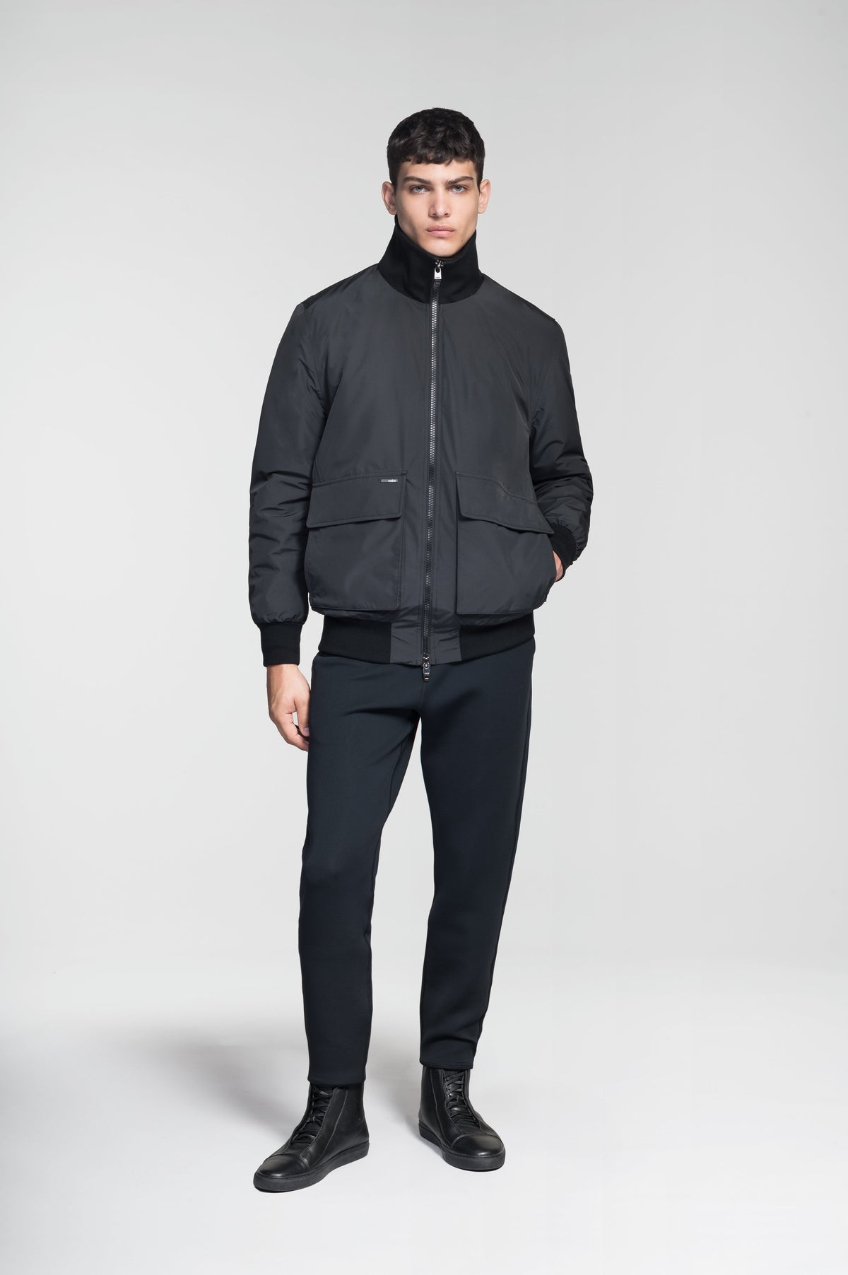 Flint Men's Tailored Rib Collar Jacket in hip length, premium 3-ply Micro Denier fabrication, premium 4-way stretch, water resistant Primaloft Gold Insulation Active +, flap pockets with magnetic closure at waist, side entry pockets at waist, ribbed sleeve cuffs, two-way branded zipper at centre front, box pleat detailing at centre back, large interior zipper pocket, and interior button pocket at left chest, in Black